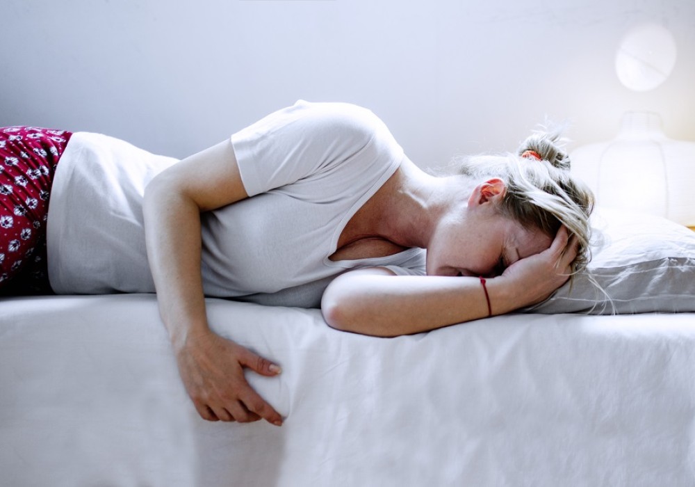 Frau liegt schmerzerfüllt mit Wärmflasche auf ihrem Bett 