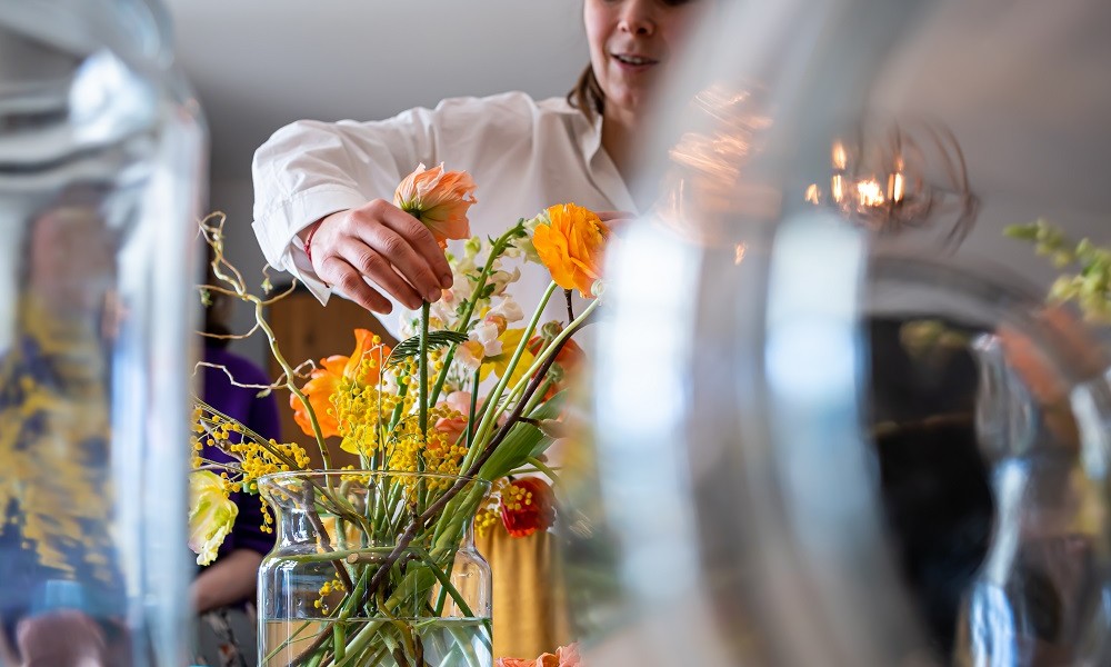 Frau, welche gerade eben dabei ist Schnittblumen in eine Vase zu geben 