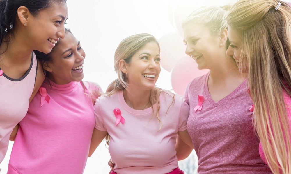 Frauen welche sich alle an den Schultern greifen und umarmen und im Zeichen des Brustkrebs alle in Pink gekleidet sind und eine pinke Schleife tragen