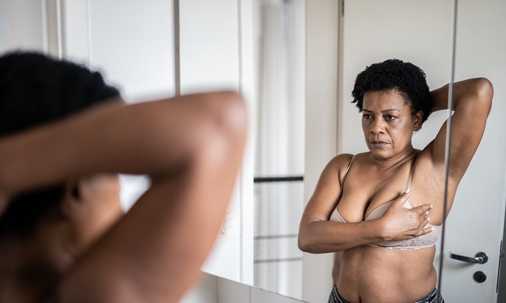 Frau im Spiegel tastet ihre Brüste zur Vorsorge gegen Brustkrebs ab
