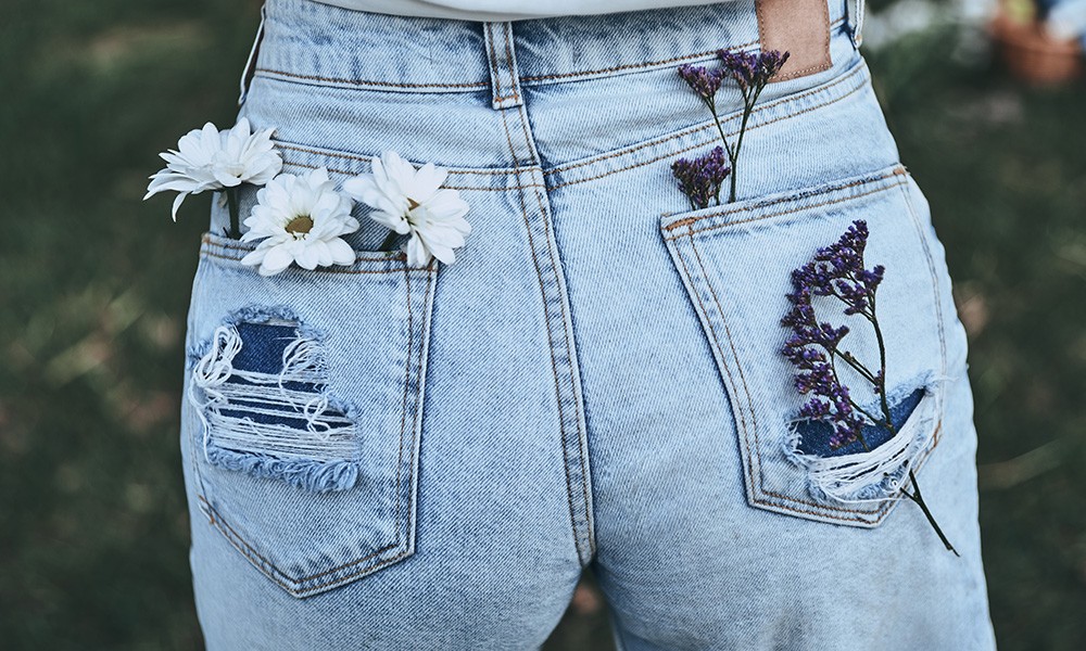 Rückseite einer blauen Jeans, in die löchrigen Taschen auf der Rückseite wurden Blumen gesteckt 